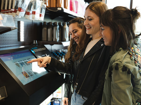 A photo of three women buying a concert ticket at a kiosk inside a gas station in Germany